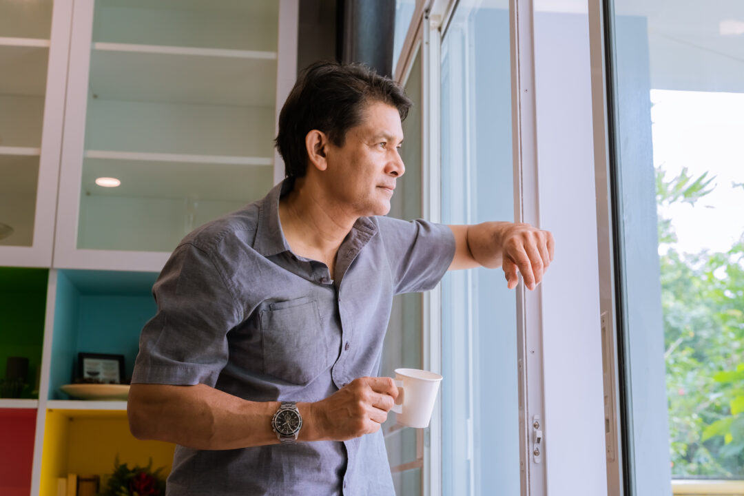 Man tittar ut genom fönstret med en kaffe och undrar om han borde få sjukersättning eller vara yrkesarbetande?